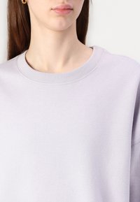 Ljuslavendelfärgad sweatshirt med ribbat rundhals, mjukt strukturerat tyg, som visar en avspänd passform och subtila sömmar.