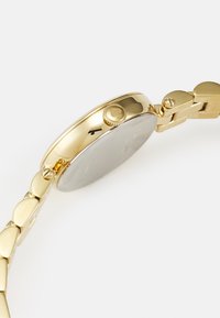Gold-tone watch featuring a round case, textured surface, and a link bracelet with polished accents. Side crown for adjustments.