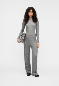 Γκρι σετ δύο τεμαχίων από απαλό ύφασμα, που περιλαμβάνει μακρυμάνικο τοπ και παντελόνι με φαρδιά μπατζάκια. Συνδυασμένο με τσάντα χειρός με σχέδιο φίδι.