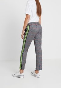Geruite broek met een neon groene zijstreep, getailleerde pasvorm en enkellengte. Gecombineerd met witte sneakers en een effen wit T-shirt.