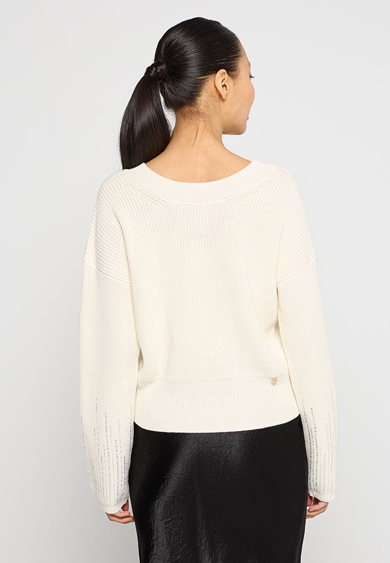 Maglione a maglia color crema con vestibilità rilassata, dettagli a coste e spalle scese. Presenta un orlo leggermente accorciato e maniche lunghe.