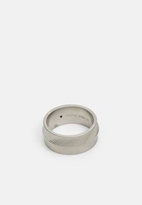 Sølv rustfrit stålring med et tekstureret, diagonalt mønster. Indersiden af ringen er mærket "FOSSIL STEEL 10." Glat overflade med let afrundet kant.