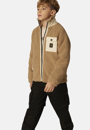 Brown fleece jacket with cream accents, zip closure, and a front pocket. Paired with black cargo pants. Smooth texture throughout.