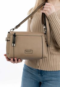 Beige leather handbag with a rectangular shape, top zipper, black accents, and adjustable strap. Features logo and textured finish.