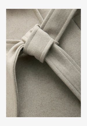 Vaaleanbeige villasekoitekangas, jossa on solmittu yksityiskohta ja sileä rakenne, näkyvillä saumoilla ja minimalistisella, taitetulla muotoilulla.