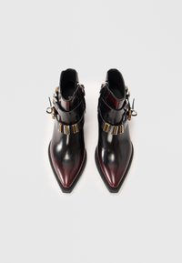 Bottines en cuir noir verni avec des orteils pointus, des accents décoratifs en métal doré et argenté, et des sangles à double boucle.