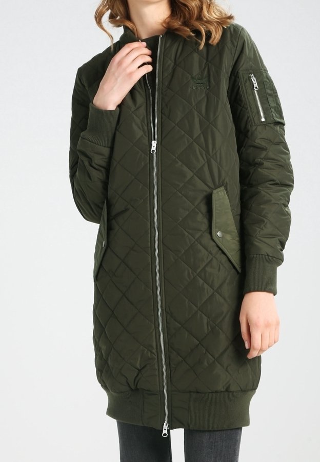 Quilted green long jacket with zip closure, ribbed cuffs, and side pockets. Features a zippered sleeve pocket and a smooth texture.