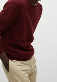 Maglione a maglia color bordeaux con scollatura tonda e polsini a costine, abbinato a pantaloni beige, caratterizzati da una texture liscia e una vestibilità comoda.