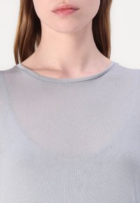 Haut léger gris clair, transparent, avec un col rond et une texture lisse, à coupe ajustée et de subtils détails de tissage.