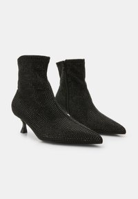 Botines negros de tobillo con puntera puntiaguda, cubiertos de pequeños cristales, con cierre de cremallera en el lateral y tacón de tipo kitten.