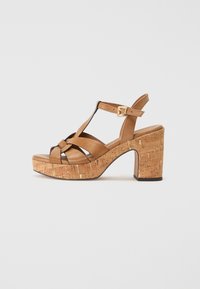 Sandali platform in pelle marrone con tacco a blocco in sughero. Presentano cinturini incrociati e una cinghia alla caviglia regolabile con una fibbia dorata.
