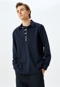 Marinefarbener Viertelreißverschluss-Pullover aus leichtem Stoff, mit Kragen und langen Ärmeln. Dezenter Glanz und lässige Passform.