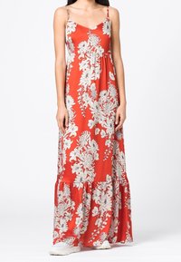 Červené květinové maxi šaty s bílými botanickými vzory, nastavitelné tenké ramínka, volánový lem a lehký materiál.