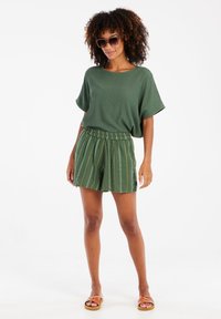 Haut à manches courtes vert à côtes associé à un short vert à motifs avec une taille élastique, et des sandales à lanières marron.