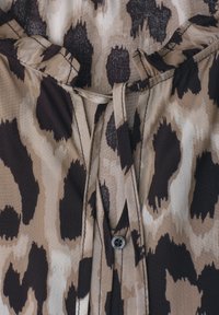 Tissu imprimé animal marron et beige avec un lien à l’avant et un petit détail de bouton noir sur un matériau léger.