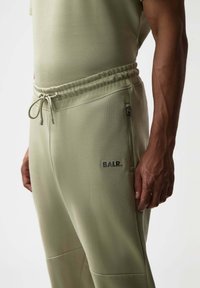 Lichtgroene jogger broek met een trekkoord in de taille, ritssluiting aan de zijkanten en subtiele branding "BALR." in donkergrijs. Soepele textuur, slank ontwerp.