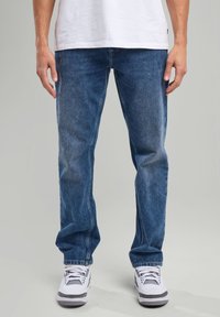 Blue denim jeans with a relaxed fit, featuring a faded finish, five-pocket design, and a standard waistband. Paired with white sneakers.