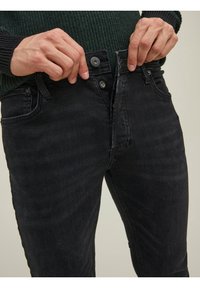 Černé džínové kalhoty s úzkým střihem, vybavené zapínáním na knoflík a zip, předními kapsami a minimálním prošíváním pro čistý vzhled.