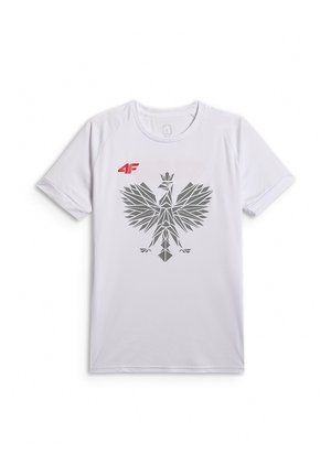Młody mężczyzna z krótkimi włosami, ubrany w białą sportową koszulkę z szarym geometrycznym emblematem orła i czerwonym logo 4F, stoi z jedną ręką w kieszeni.