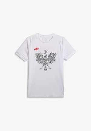 Młody mężczyzna z krótkimi włosami, ubrany w białą sportową koszulkę z szarym geometrycznym emblematem orła i czerwonym logo 4F, stoi z jedną ręką w kieszeni.