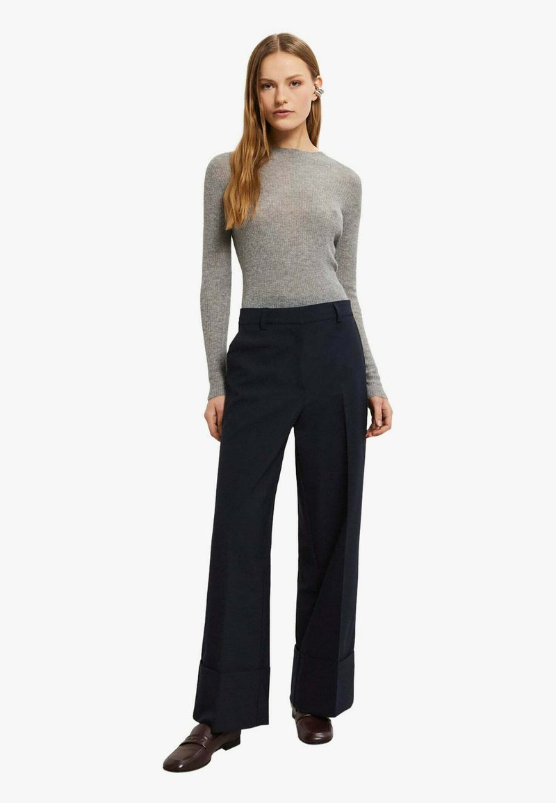 Top grigio aderente a maniche lunghe abbinato a pantaloni navy a gamba larga. I pantaloni presentano un design strutturato con orlo piegato. Scarpe marroni completano il look.