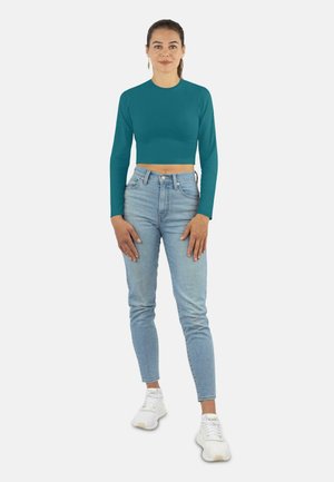 Tieferte blauer langärmliger Cropped-Top, eng anliegendes Design, kombiniert mit hoch geschnittenen, hellblauen Jeans und weißen Sneakers. Schlichte, glatte Textur, ohne Muster.