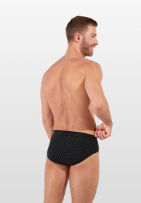 Schwarze Schwimmslips mit strukturiertem Muster, elastischem Bund und einer engen Passform. Der Stoff wirkt glatt mit geometrischen Akzenten.