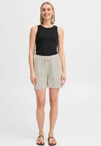 Haut sans manches noir et short rayé beige clair avec une taille élastique. Le modèle se tient en sandales devant un fond neutre.
