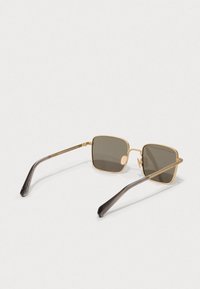 Χρυσά μεταλλικά γυαλιά ηλίου με τετράγωνους σκούρους γκρί φακούς και γκρίζες πλαστικές άκρες στους βραχίονες, καθαρές γραμμές και ελάχιστες λεπτομέρειες εξαρτημάτων.