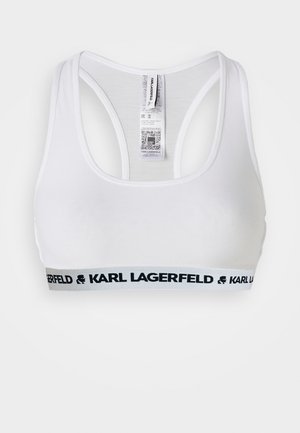 Biały krótki top z wycięciem typu racerback. Na dole znajduje się czarna elastyczna taśma z nadrukiem "KARL LAGERFELD". Gładka faktura materiału.