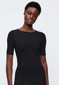 Haut ajusté à manches courtes noir en tissu texturé, avec un col rond et des coutures lisses. Épaules accentuées rigides.