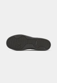 Black rubber shoe sole with textured grip pattern, featuring a flat shape and reinforced areas for durability. Features a central logo detail.