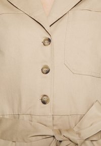 Beige bavlněná košile s límečkem, pěti kulatými knoflíky, kapsou na prsou a detailem s uvázaným pasem, s hladkou texturou a zakázkovým střihem.