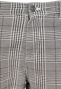 Schwarz-weißer Karostoff mit unterschiedlichen Mustern und Texturen, der an der Taille mit einem Metallknopf und einem Reißverschluss ausgestattet ist.