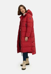 Red puffer coat with a hood, zip and snap closure, vertical quilting, side pockets, and a black lining; paired with beige lace-up boots.