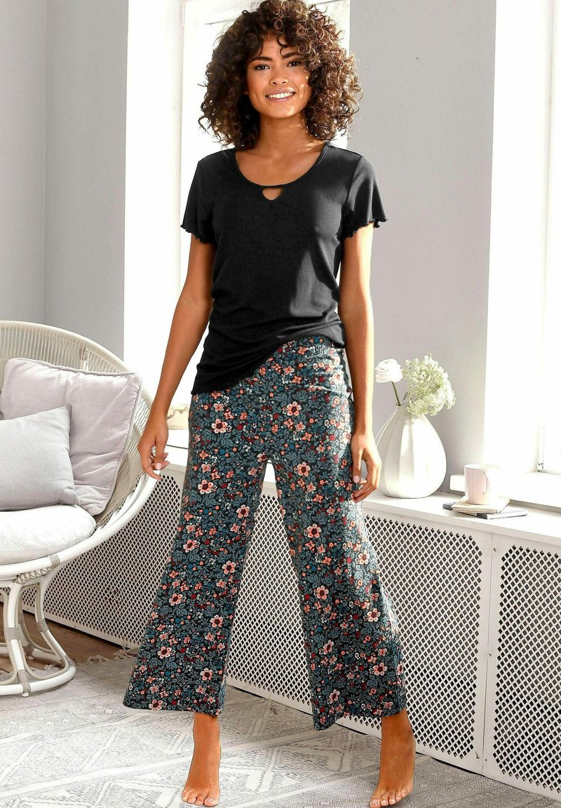 Black short-sleeve top with a keyhole detail and frayed edges paired with wide-leg floral print pants in dark blue, pink, and white.
