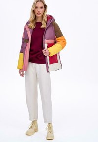Kolorowa kurtka puchowa z kapturem, z różowymi, brązowymi i pomarańczowymi panelami. Połączona z burgundowym swetrem i kremowymi spodniami oraz beżowymi botkami.