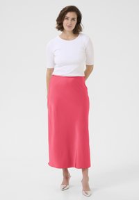 Falda maxi de satén rosa con una textura suave, complementada con una blusa blanca ajustada. El conjunto se acompaña de unos zapatos de punta de color claro.