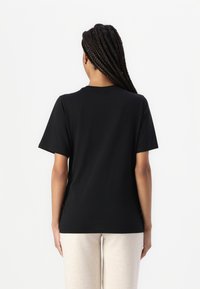 Black cotton t-shirt featuring short sleeves, a crew neck, and a relaxed fit, paired with light beige sweatpants.