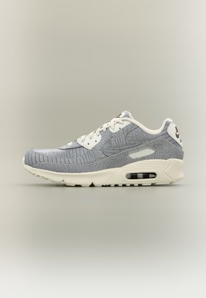 Szaro-biała teksturowana tenisówka z widoczną podeszwą z poduszką powietrzną, wiązaniem na sznurówki oraz subtelnym logo Nike Swoosh po boku na neutralnym tle.