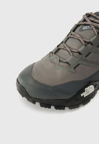 Szare buty trekkingowe z teksturowaną cholewką, wzmocnionym noskiem i wytrzymałą podeszwą z wyraźnym bieżnikiem. Logo marki na boku.