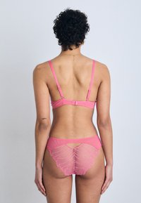 Conjunto de lingerie rosa composto por um sutiã de tecido suave com alças ajustáveis e uma lingerie combinando com detalhes em renda e um design recortado.