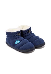 Zapatillas de corduroy azul con un interior de felpa blanca, diseño acolchado, suela negra y detalle de cierre tipo toggle. Logo en azul claro en el lateral.