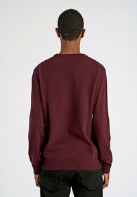 Bordeaux trui met een geribbelde ronde hals, lange mouwen en een zachte textuur, weergegeven tegen een neutrale achtergrond.