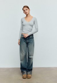 Svijetlosiva rebrasta majica s dugim rukavima i izrezom nazubljenog ruba, uparena s izblijedelim širokim trapericama i bež platformama.