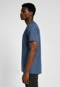 Marineblauw T-shirt met korte mouwen in een katoenmix, met een borstzak en een relaxte pasvorm, getoond op een model van opzij.