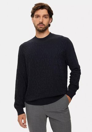 Maglione nero con un design texturizzato caratterizzato da un motivo ripetuto del nome del marchio. Polsini e orlo a coste, collo rotondo e maniche lunghe.