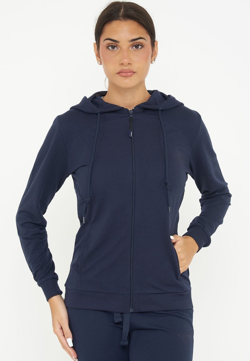 Felpa con zip di colore navy, dotata di cappuccio con coulisse, polsini e orlo a costine, caratterizzata da una texture di tessuto liscia e tasche laterali.