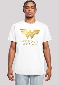 Balts kokvilnas T-krekls ar lielu zeltītu "Wonder Woman" logo, kas papildināts ar spārnu akcentiem. Parastā griezuma ar īsām piedurknēm un apaļu kakla izgriezumu.