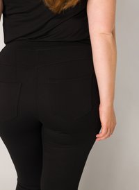 Zwarte legging gemaakt van rekbaar materiaal met een gladde textuur, voorzien van een hoge tailleband en twee achterzakken.